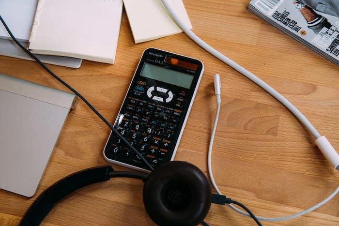 Calculator on a wooden table with headphones and various notepads