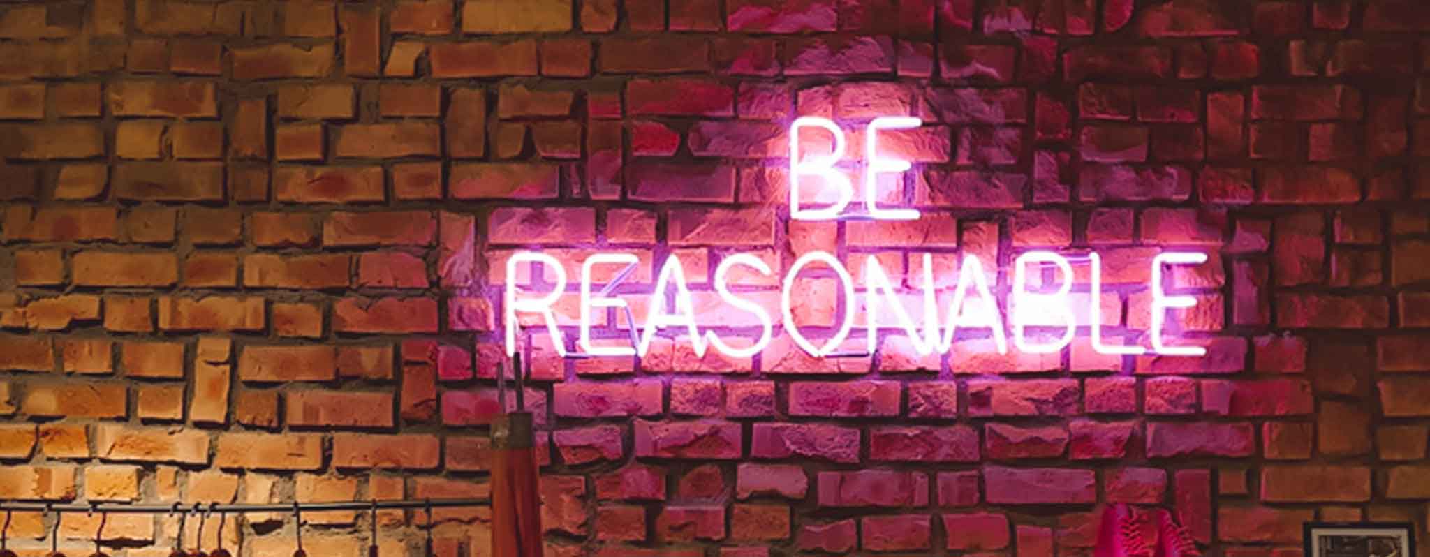 a sign that says be reasonable in front of a brick wall 