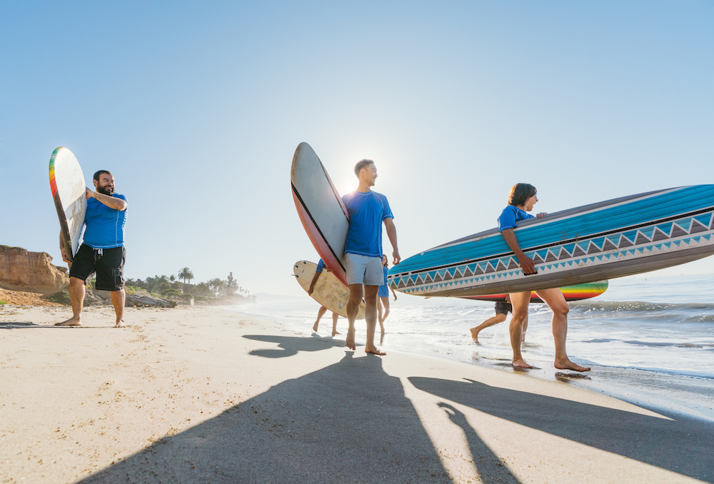 outdoors on the beach with three surfers holding boards